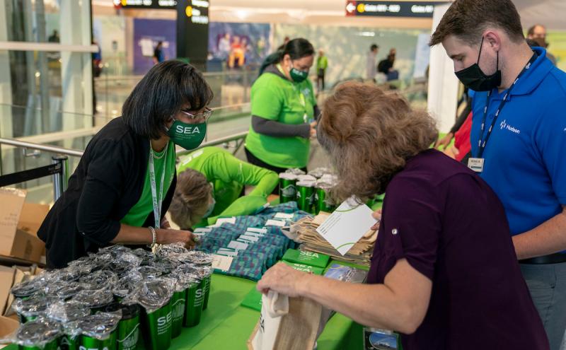 People at an airport event table distributing SEA‑branded items and informational materials.