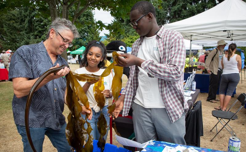 A young man and woman interact with Commissioner Felleman at the Duwamish River Festival.