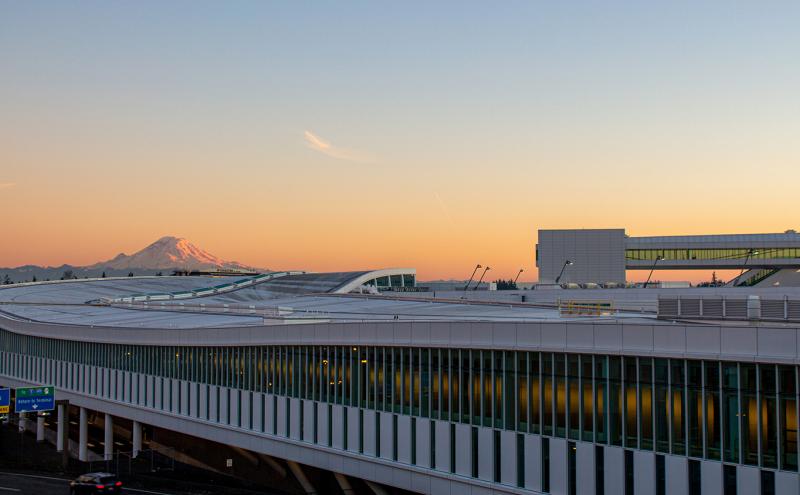 Southward, exterior view of the new International Arrivals Facility at SEA against an orange sunset silhouetting Mt Rainier 