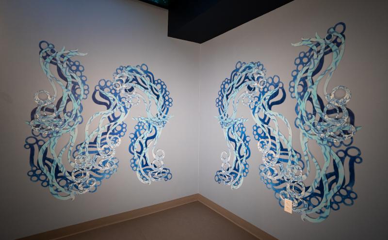 Two mirrored wall installations of flowing blue serpentine forms installed in a corner of the SEA Airport.