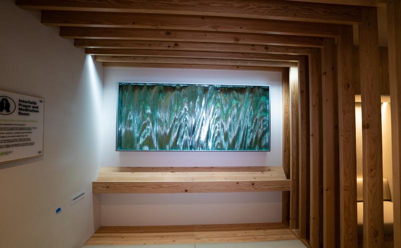 A backlit panel mounted in a wood-framed alcove inside SEA Airport Interfaith Prayer and Meditation room. 
