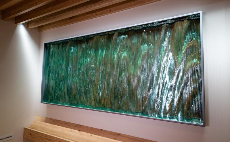Full view of the framed glass panel mounted on the wall above the wooden bench. 