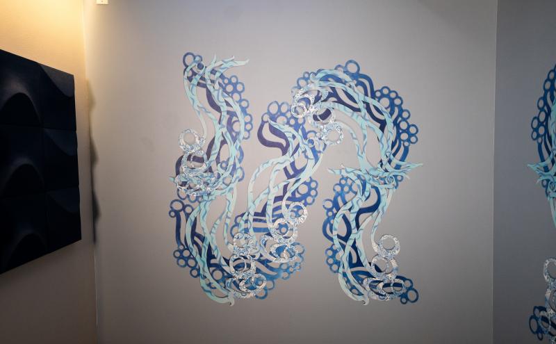 A closer view of one wall panel showing intertwining blue serpentine forms with layered rings and curling tendrils. 