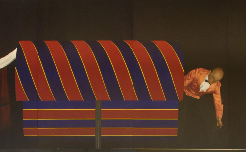 Painted panel showing the assistant peering into the striped box, with a handing appearing at the left edge. 