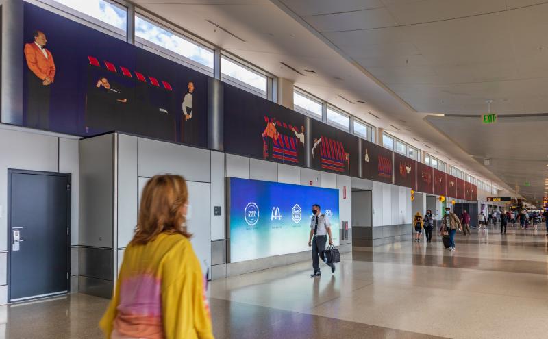 A photorealistic mural running the full length of the airport concourse wall, depicting sequential scenes of a magician and assistant.