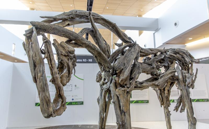 Close-up side view of the horse sculpture showing the texture and construction of the interlocking branches forming the body and neck. 