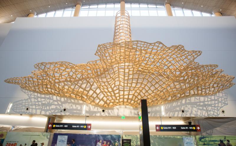 A large cantilevered wood sculpture spanning the ceiling of SEA Airport North Satellite concourse, viewed from below.