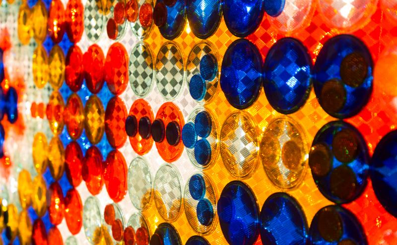 Rows of large overlapping circular reflectors, each with a faceted geometric pattern on it's surface, mounted against a backlit wall.
