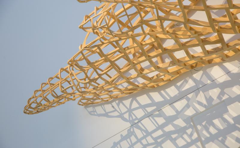 Close-up detail of the woven cedar lattice structure casting a geometric shadow on the wall behind it. 