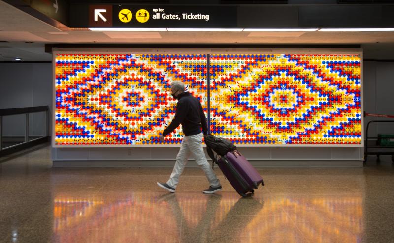 A traveler with rolling luggage walking past the two-panel installation, the artwork spanning the full width of the wall behind them.