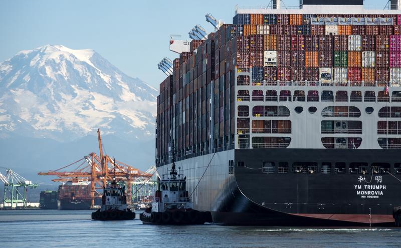 A pilot tug guides a huge cargo ship into the Tacoma harbor with Mt Rainier prominently in the sky