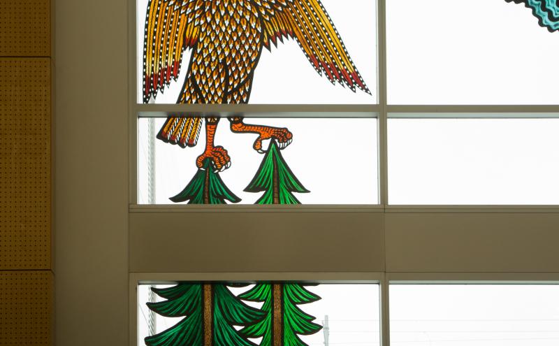 A large eagle with detailed feather patterning, it's talons gripping two evergreen trees. 