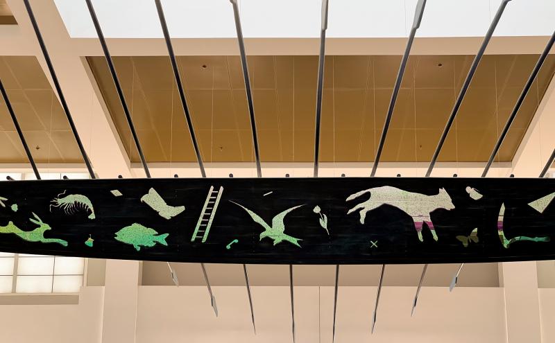 Middle half of boat with cut-outs in the sides of the boat reveal images of tools, plants, and animals.