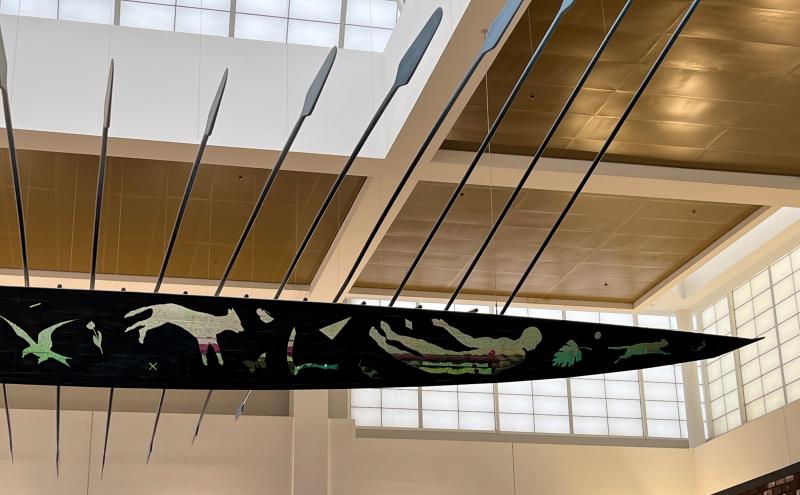 End half of boat with cut-outs in the sides of the boat reveal images of tools, plants, and animals.