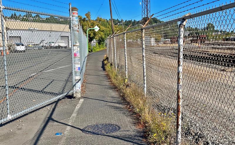 Narrow T-91 Trail segment between fences along the rail yard