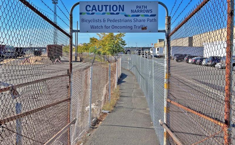Narrow T-91 trail segment with a caution sign reading 'path narrows bicyclists and pedestrians share patch, watch for oncoming traffic