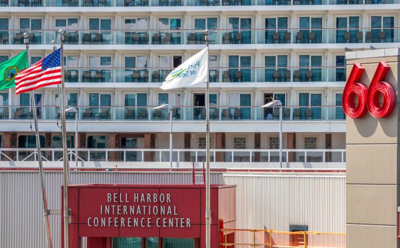 Flags in front of the Bell Harbor International Conference Center with a large cruise ship docked behind the building.