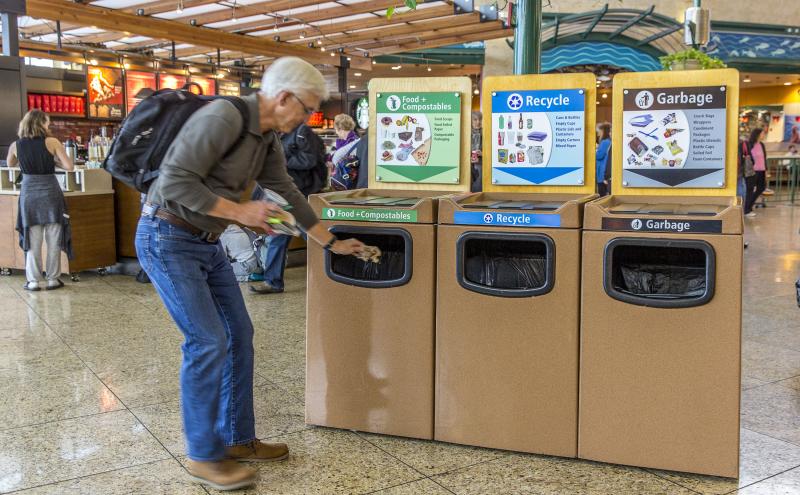 Man discards compost items at bin in an airport terminal.