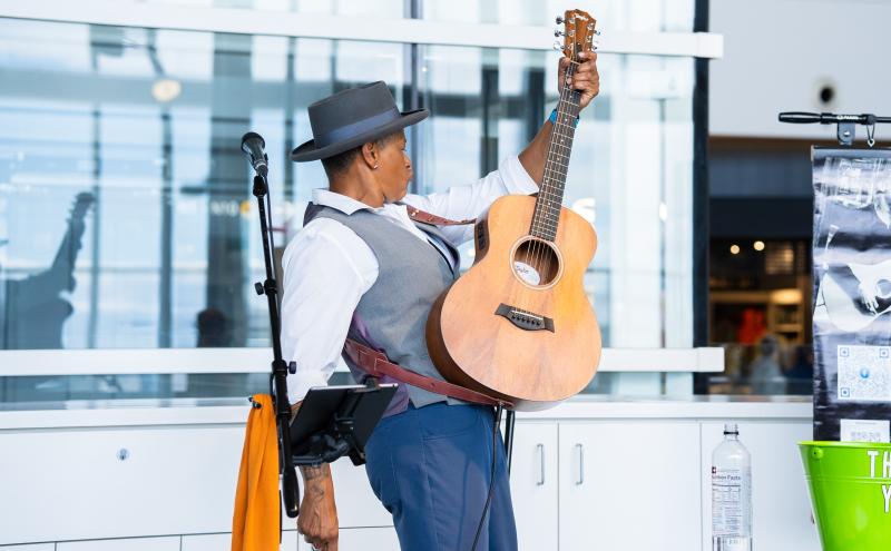 Kim Archer energetically playing the guitar and singing at Marketplace in N Concourse. 