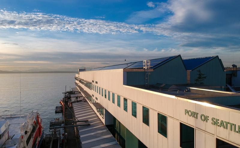 Waterfront building marked “Port of Seattle” beside a docked vessel, with a wide view of the water and sky at sunset.