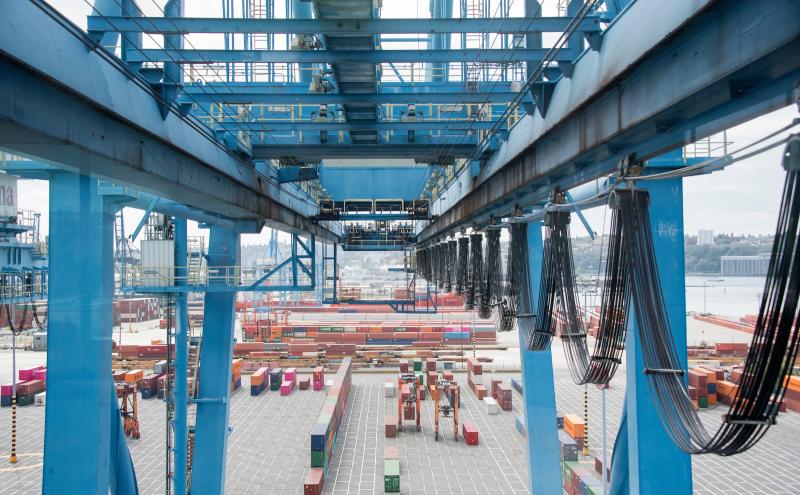 A large blue gantry crane over a shipping yard with rows of cargo containers.