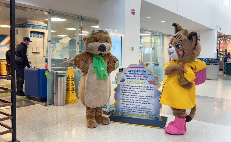 Jett the SEA Otter stands with other costumed cat character next to the play area rules.