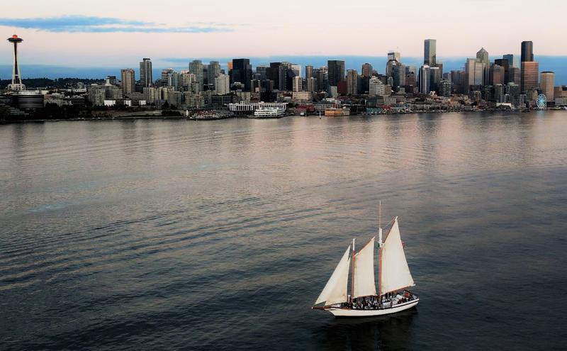 The Bay Lady sailboat moves across calm water with a city skyline in the background.