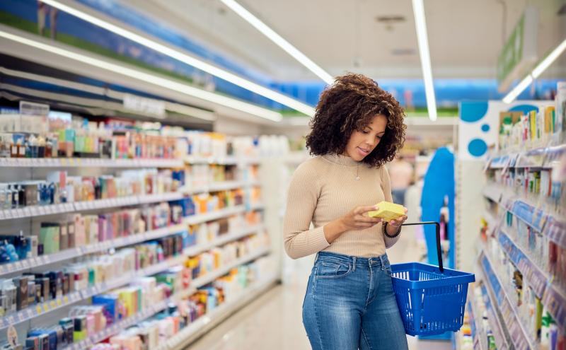 Shopper examining an item in a brightly lit retail aisle with a blue basket.