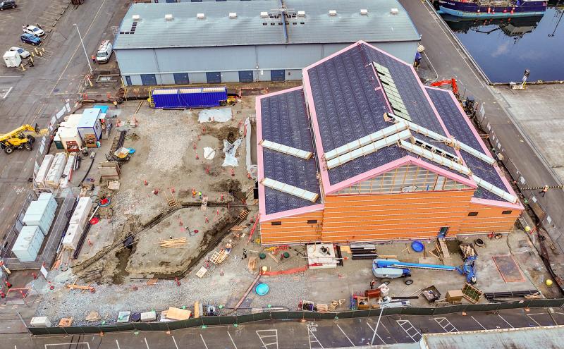 Aerial view of a construction site with an unfinished building surrounded by equipment, materials, and fenced-off work areas.