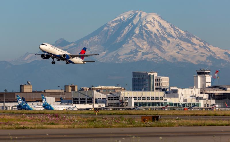 A commercial jet takes off from SEA Airport, with Mt. Rainier in the background