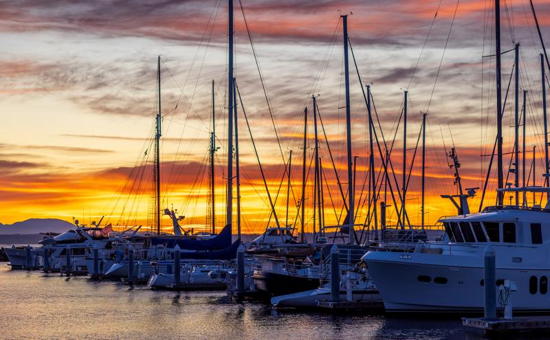 Sailboats and yachts docked at Shilshole Bay Marina at twilight, with a colorful sunset sky behind them.