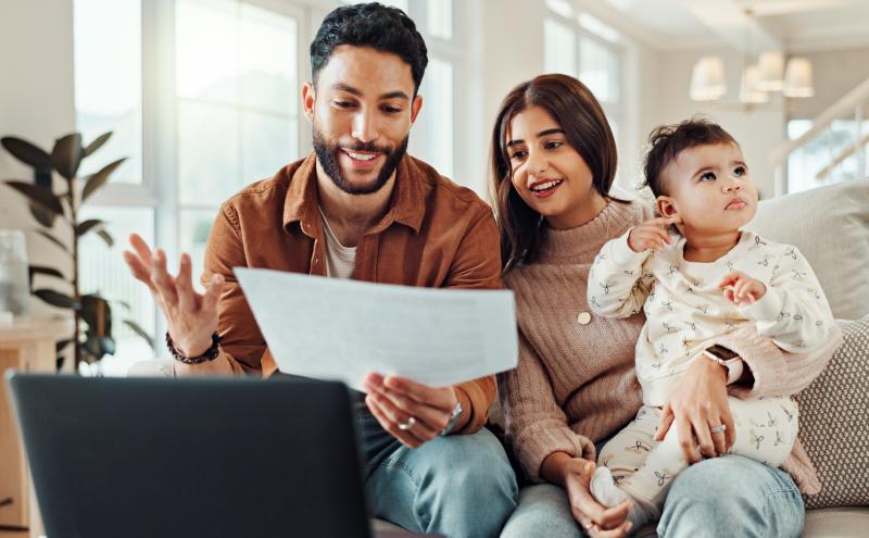 Parents discuss a document over an open laptop while mom holds baby