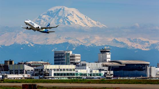 A view of Sea-Tac Airport looking southeast toward Mt. Rainier, as a jet takes off in the foreground.