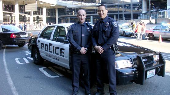 Two officers standing in front of a police car.