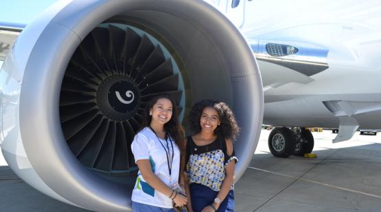 Two interns happily pose by an airplane turbine.