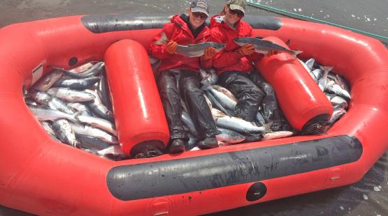 Evelyn Clark next to friend holding salmon in fishing raft.
