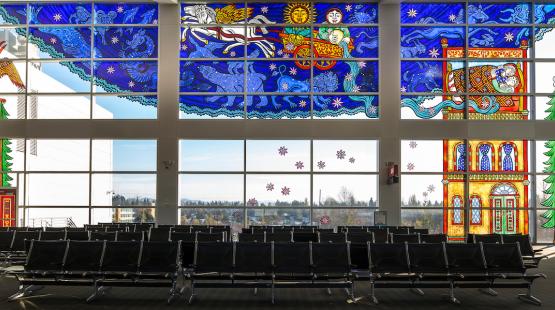 Full stained glass window spanning the upper portion of the airport gate wall, with clear windows and seating below.