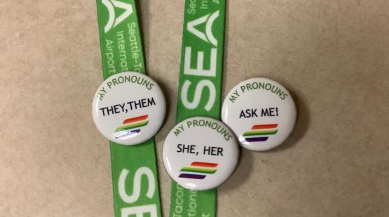 Buttons with personal pronouns on a SEA Airport lanyard.