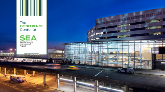 Exterior view of a brightly lit glass-walled building at SEA Airport during dusk, with vehicles moving along the roadway in the foreground. On the left side of the image, a vertical banner displays the text “The Conference Center at SEA – Seattle–Tacoma International Airport” alongside a green stylized graphic.