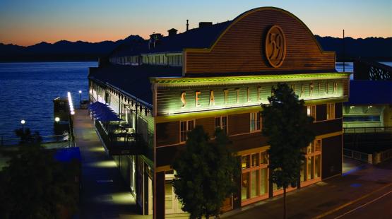 Dusk Seattle Aquarium facility at Pier 59 with orange and pink sky and blue water of Elliott Bay