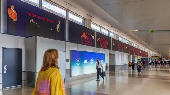 A photorealistic mural running the full length of the airport concourse wall, depicting sequential scenes of a magician and assistant.