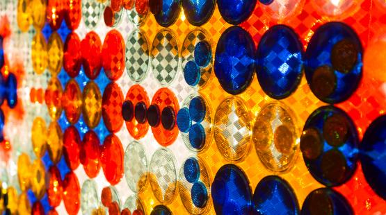 Rows of large overlapping circular reflectors, each with a faceted geometric pattern on it's surface, mounted against a backlit wall.