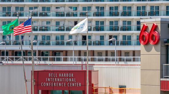 Flags in front of the Bell Harbor International Conference Center with a large cruise ship docked behind the building.