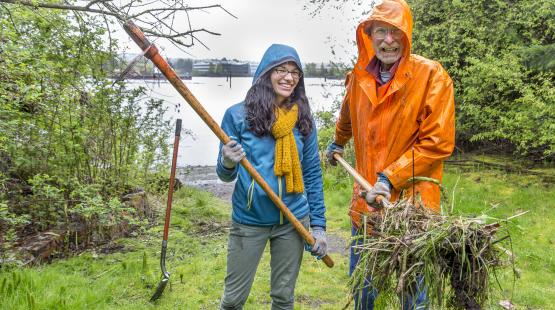 Two port staff members clean up park along the Duwamish with shovel 