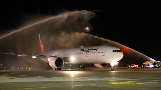 A Philippines‑branded airplane on a runway at night receives a water‑spray salute from airport fire trucks.