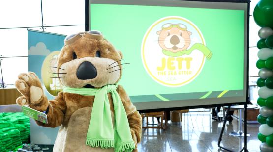 Photograph of costumed SEA Airport mascot Jett the SEA Otter, a sea otter with a green scarf and aviator goggles