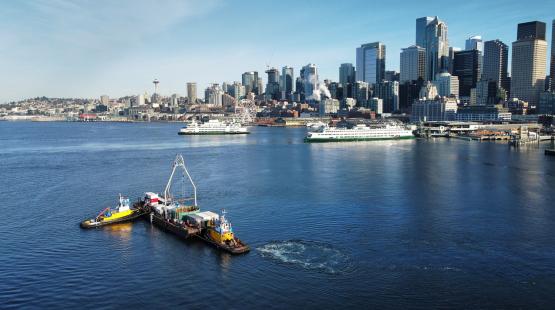 Seattle waterfront with ferries on the water and small work vessels in the foreground.