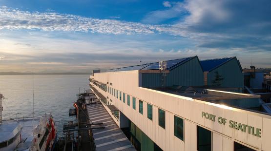 Waterfront building marked “Port of Seattle” beside a docked vessel, with a wide view of the water and sky at sunset.