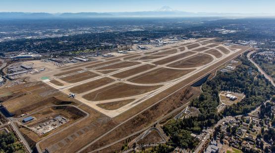 An aerial view of SEA with multiple runways, taxiways, terminals, and surrounding city and landscape.