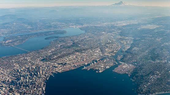 High-altitude aerial view of a coastal city with lakes, waterways, and a distant snow-capped mountain.